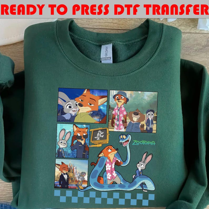 May include: A dark green sweatshirt featuring a colorful graphic of characters from the animated movie "Zootopia." The graphic includes images of a fox, a rabbit, and other animal characters in various scenes. The text "Zootopia" is also visible.
