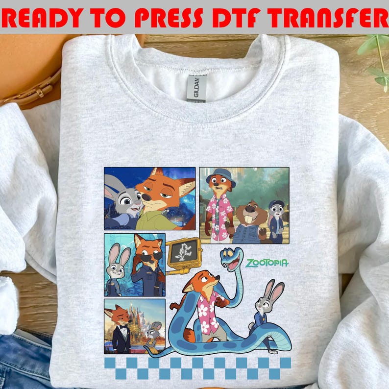 May include: A light gray sweatshirt featuring a colorful graphic of characters from the animated movie "Zootopia." The design includes multiple panels with images of a fox, a rabbit, and other characters. The text "READY TO PRESS DTF TRANSFER" is at the top.