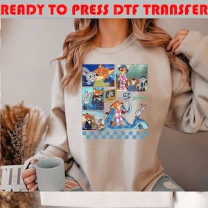 May include: Beige sweatshirt featuring a colorful comic strip design with characters from the animated movie Zootopia. The design includes images of a fox, a bunny, and other characters. The text "READY TO PRESS DTF TRANSFER" is at the top.