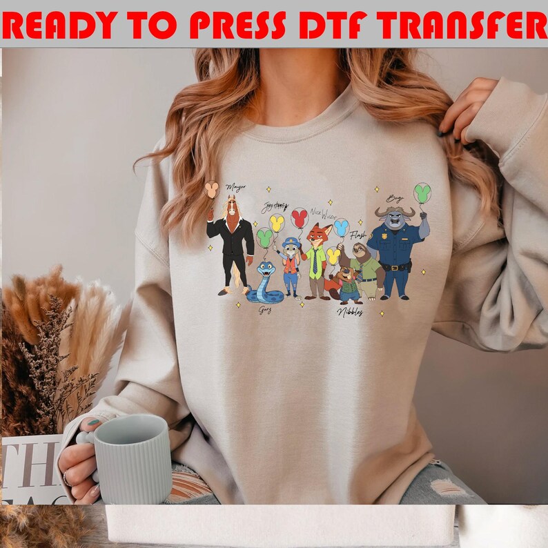 Peut inclure: Sweat-shirt beige avec un graphisme de dessin anim&eacute; color&eacute; de personnages de film. Le graphisme comprend un cheval, un serpent, un renard et un paresseux, chacun tenant un ballon. Le texte en haut indique "READY TO PRESS DTF TRANSFER."
