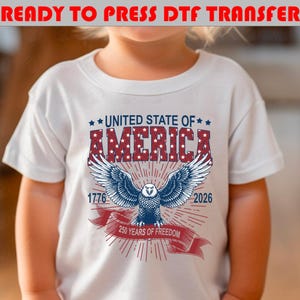 Op de afbeelding: Een wit t-shirt met een afbeelding van een Amerikaanse zeearend met gespreide vleugels. Boven de adelaar staat de tekst UNITED STATE OF AMERICA in rood en blauw. De jaartallen 1776 en 2026 staan naast de adelaar, met een rood lint 250 YEARS OF FREEDOM.
