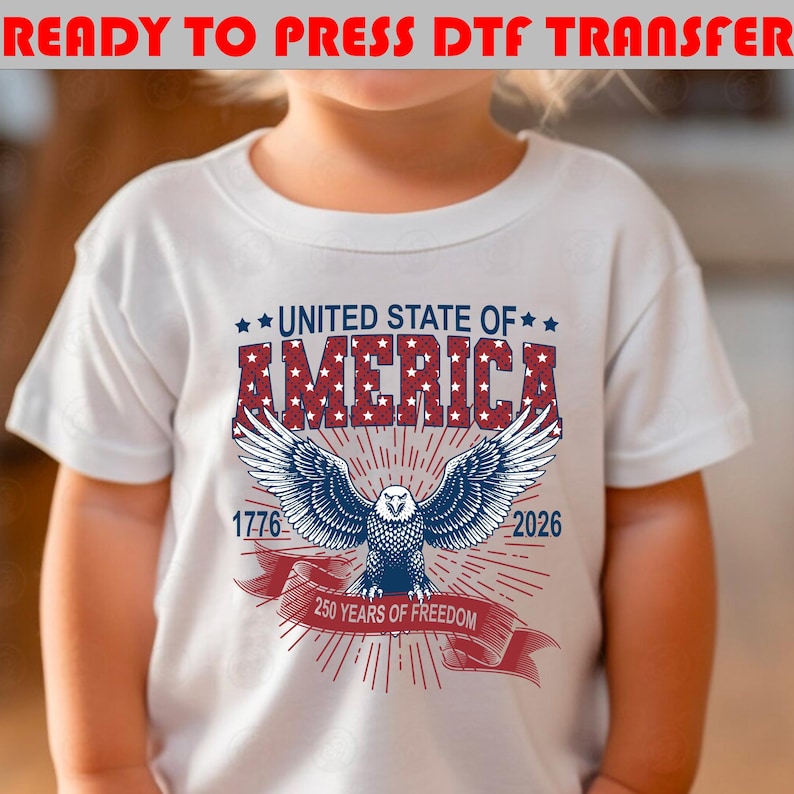 Op de afbeelding: Een wit t-shirt met een afbeelding van een Amerikaanse zeearend met gespreide vleugels. Boven de adelaar staat de tekst UNITED STATE OF AMERICA in rood en blauw. De jaartallen 1776 en 2026 staan naast de adelaar, met een rood lint 250 YEARS OF FREEDOM.