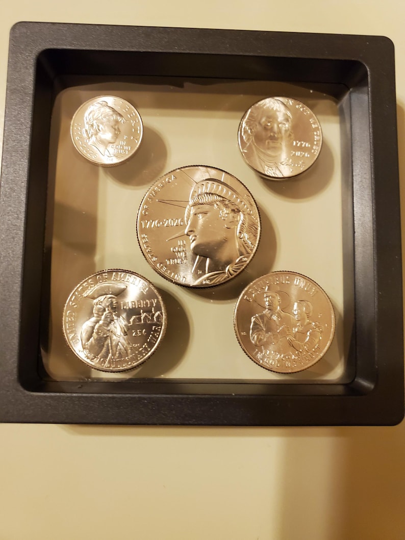 May include: A collection of five silver coins displayed in a black shadow box. The coins feature portraits and historical dates. The largest coin depicts the Statue of Liberty. The coins are encased in a clear, protective display.