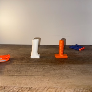 May include: An orange and black toy gun, a white boot-shaped object, an orange cylindrical object, and three blue and orange toy darts are arranged on a wooden surface. The objects are likely toy accessories.