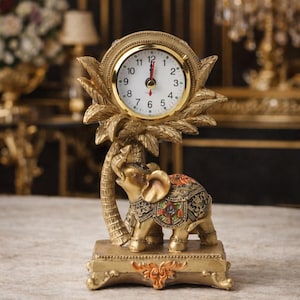 May include: A gold-coloured decorative clock featuring an elephant figurine. The clock face is round with black numerals and hands. The elephant is adorned with colourful patterns. The clock is set on a rectangular base.