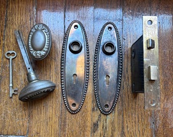 Juego completo de herrajes para puertas con pomos y placas traseras ovalados con acabado en cobre antiguo.