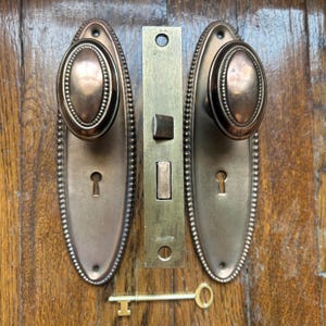 Juego de herrajes de latón antiguo para puertas: pomos ovalados, placas de montaje y cerradura de embutir (acabado color cobre).