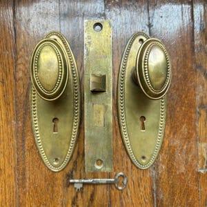 Juego de herrajes de latón antiguo para puertas: pomos ovalados, placas de montaje y cerradura de embutir.
