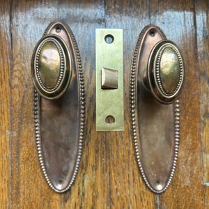 Juego de herrajes de latón antiguo para puertas: pomos ovalados, placas de montaje y pestillo.