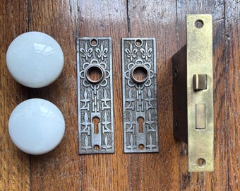 Juego de herrajes antiguos para puertas con diseño de flor de lis, pomos de porcelana y placas traseras de hierro fundido.