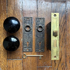 Zestaw antycznych, estetycznych okuć drzwiowych z czarnymi porcelanowymi gałkami, żeliwnymi płytkami tylnymi i mosiężnym zamkiem wpuszczanym