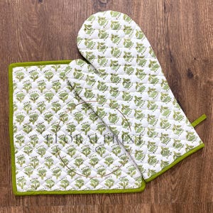 May include: White quilted oven mitt and pot holder set with a green floral pattern and green trim. The kitchen textiles are made of a soft material and are designed for heat resistance. The set is perfect for cooking and baking.