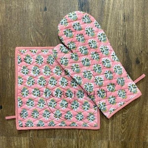 Può includere: Un set di presina e guanto da forno trapuntati. Il set presenta uno sfondo rosa con un motivo floreale ripetuto in tonalità di blu, giallo e verde. I bordi sono rifiniti con un bordo rosa abbinato.