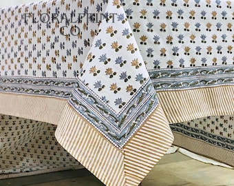 May include: A white tablecloth with a repeating floral pattern in blue and gold. The border features a blue and white design with a striped tan edge. The tablecloth is draped over a table.