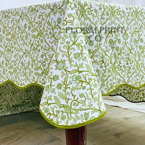 May include: White tablecloth with a green floral pattern and a green border. The tablecloth is draped over a table, showcasing the intricate design. The text "FLORAL PRINT CO" is visible on the tablecloth.