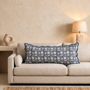 May include: A long rectangular lumbar pillow featuring a dark blue and off-white floral block print pattern. The pillow has a scalloped edge finished with dark blue piping and is positioned horizontally across a light beige upholstered sofa.