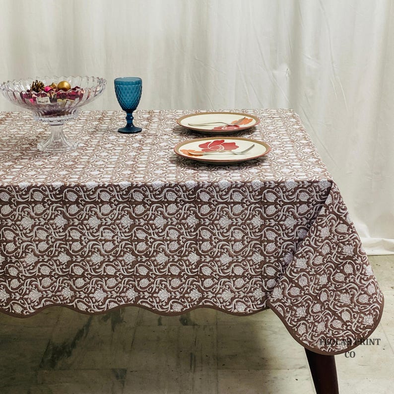 Authentic Indian hand block print cotton tablecloth in rich Mud Brown tones featuring floral patterns and matching piping border. This reusable dining table linen is beautifully styled with layered plates, candles, and greenery to create an inviting boho farmhouse atmosphere for weddings, dinner parties, brunch gatherings, seasonal décor, and elegant home entertaining.