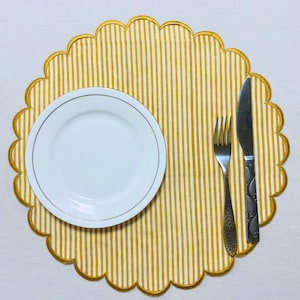 Può includere: Un piatto bianco con bordo dorato è appoggiato su un sottopiatto a righe gialle e bianche con bordo smerlato. Una forchetta e un coltello sono posizionati a destra del piatto. Il sottopiatto ha un bordo dorato.