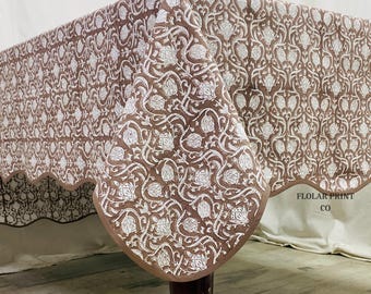 May include: A brown and white floral patterned tablecloth with a scalloped edge. The tablecloth is draped over a table, showcasing the intricate design. The text "FLOLAR PRINT CO" is visible on the edge.