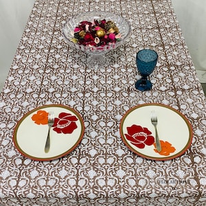 Rectangular Mud Brown cotton tablecloth with detailed floral hand block print and matching piping border spread across a farmhouse dining table. The handmade reusable table linen showcases authentic artisan craftsmanship and soft breathable cotton fabric, making it ideal for wedding table décor, seasonal gatherings, dinner parties, family meals, kitchen styling, and bohemian-inspired home decoration.