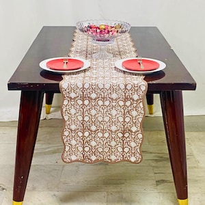 Peut inclure: Une table à manger en bois brun foncé avec un chemin de table à motifs floraux, deux assiettes rouges et un bol en verre transparent rempli d'objets décoratifs. Les pieds de la table ont des accents dorés. Le texte "FLORALPRINT CO." est visible.