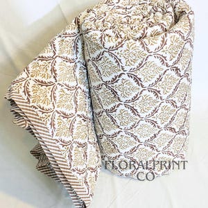 Floral reversible quilt handmade from breathable cotton and finished with charming block print patterns. Designed for all season comfort, it works as a light summer blanket or layered winter cover. Use it on a couch, daybed, or bedroom bedspread for instant style. Soft fabric and artisan details make it a treasured home essential or thoughtful gift.