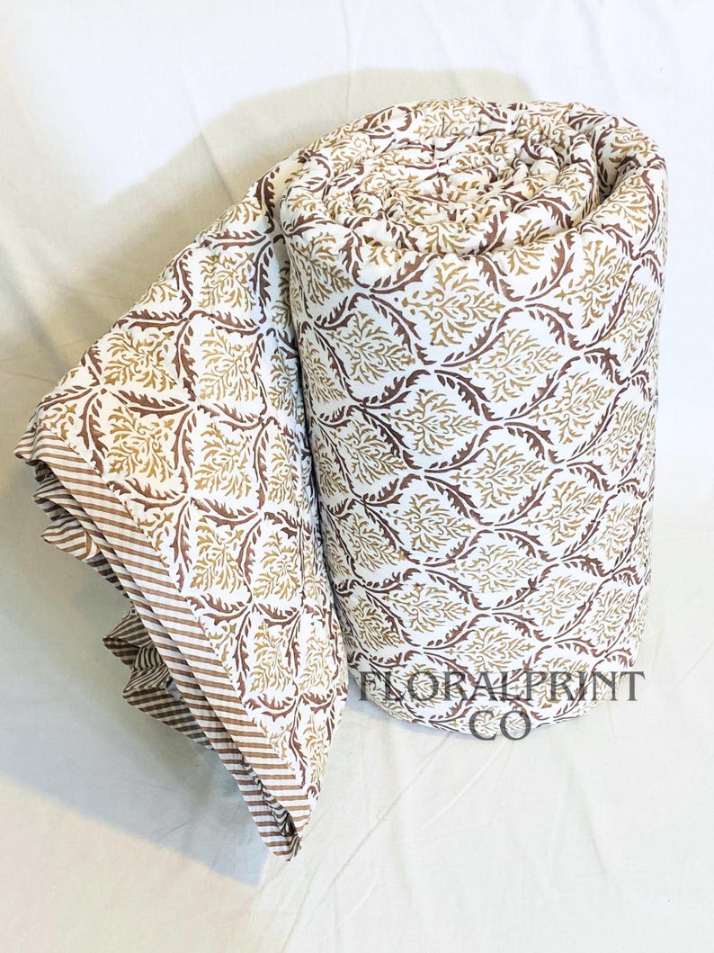 Floral reversible quilt handmade from breathable cotton and finished with charming block print patterns. Designed for all season comfort, it works as a light summer blanket or layered winter cover. Use it on a couch, daybed, or bedroom bedspread for instant style. Soft fabric and artisan details make it a treasured home essential or thoughtful gift.