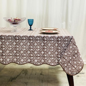 Handcrafted Mud Brown hand block print cotton tablecloth displayed on a rectangular dining table with elegant matching piping edges. The floral boho pattern creates a warm farmhouse-inspired table setting perfect for family dinners, wedding receptions, festive gatherings, and rustic home décor. Soft natural cotton fabric adds an earthy charm while complementing wooden dining furniture, neutral interiors, and cozy seasonal styling for everyday dining and special occasions.