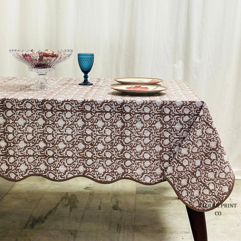Handcrafted Mud Brown hand block print cotton tablecloth displayed on a rectangular dining table with elegant matching piping edges. The floral boho pattern creates a warm farmhouse-inspired table setting perfect for family dinners, wedding receptions, festive gatherings, and rustic home décor. Soft natural cotton fabric adds an earthy charm while complementing wooden dining furniture, neutral interiors, and cozy seasonal styling for everyday dining and special occasions.