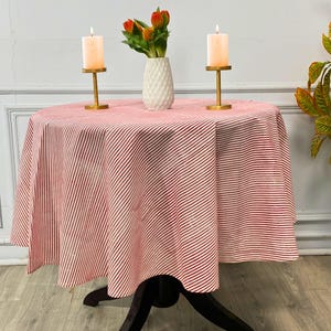Puede incluir: Una mesa redonda cubierta con un mantel a rayas rojas y blancas. Dos candelabros dorados con velas encendidas y un jarrón blanco con flores naranjas están sobre la mesa. La mesa tiene una base negra.