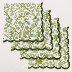 May include: Four white cloth napkins with a green floral pattern and scalloped edges. The napkins feature a repeating design of stylized flowers and leaves in shades of green.