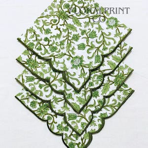 Peut inclure: Quatre serviettes en tissu blanches empilées avec un motif floral vert. Les serviettes ont un bord festonné avec une bordure vert foncé. Le motif floral comprend des feuilles et des fleurs. Le texte "FLORAL PRINT CO" est visible.