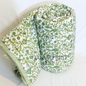 Può includere: Trapunta arrotolata con stampa floreale bianca e verde. La trapunta presenta un motivo ripetuto di foglie e fiori verdi su sfondo bianco. Il bordo della trapunta ha un bordo a righe verdi e bianche. Il testo "FLORAL PRINT CO" è visibile.