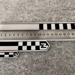 K&ouml;nnte beinhalten: Ein Satz schwarz-wei&szlig;er Lineale und ein Schl&uuml;sselanh&auml;nger mit einem schwarz-wei&szlig;en Schachbrettmuster und dem Buchstaben "Z". Das gr&ouml;&szlig;te Lineal misst bis zu 20 cm. Das Bild enth&auml;lt auch ein kleineres Lineal.