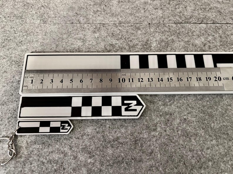 K&ouml;nnte beinhalten: Ein Satz schwarz-wei&szlig;er Lineale und ein Schl&uuml;sselanh&auml;nger mit einem schwarz-wei&szlig;en Schachbrettmuster und dem Buchstaben "Z". Das gr&ouml;&szlig;te Lineal misst bis zu 20 cm. Das Bild enth&auml;lt auch ein kleineres Lineal.