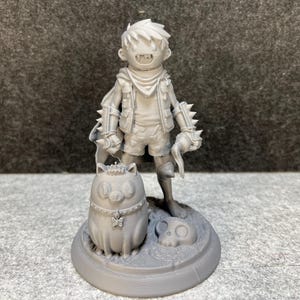 Op de afbeelding: Een grijze 3D-geprinte figuur van een jong personage met stekelige handschoenen, die een gebogen mes vasthoudt. De figuur staat op een cirkelvormige basis met een schedel en een katachtig wezen. Fantasiethema.