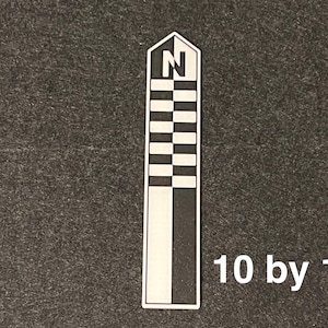 K&ouml;nnte beinhalten: Ein wei&szlig;es und schwarzes rechteckiges Objekt mit einer stilisierten Windrose oben und dem Buchstaben "N". Das Objekt hat ein Schachbrettmuster und den Text "10 by 10" in Wei&szlig;.