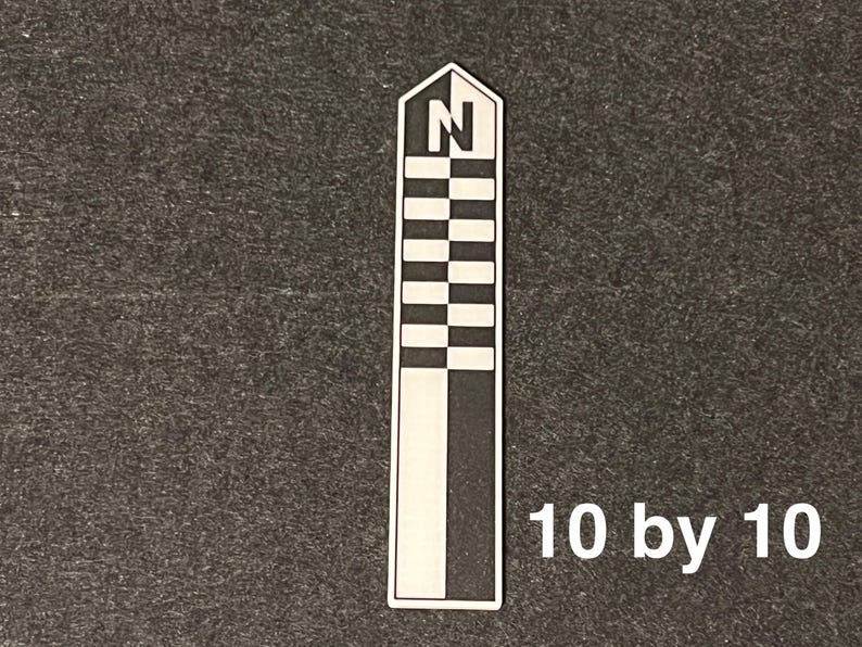 K&ouml;nnte beinhalten: Ein wei&szlig;es und schwarzes rechteckiges Objekt mit einer stilisierten Windrose oben und dem Buchstaben "N". Das Objekt hat ein Schachbrettmuster und den Text "10 by 10" in Wei&szlig;.