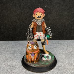 Op de afbeelding: Gedetailleerd beeldje van een stripfiguur met rood haar, een bruin vest, een korte broek met hartjespatroon en handschoenen met spikes. Een kat met een kroon en een schedel maken ook deel uit van het beeldje.