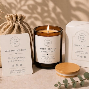Puede incluir: Una vela perfumada encendida en un frasco de vidrio marrón con tapa de madera, una caja blanca y una pequeña bolsa de arpillera. La etiqueta de la vela dice "Your Brand Name Here". Una tarjeta dice "Gracias por ser parte de nuestro viaje."