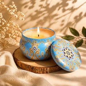 Peut inclure: Une bougie allumée dans un pot bleu orné d'un motif floral. La bougie est posée sur un dessous de plat en bois, avec le couvercle à côté. La flamme brille sur un fond chaleureux.