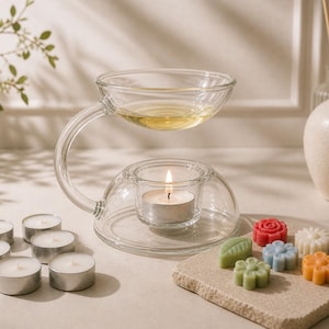 Peut inclure: Un diffuseur d'huiles essentielles en verre transparent avec une bougie allumée et un petit plat d'huile. Plusieurs bougies chauffe-plat et des fondants parfumés colorés en forme de fleurs sont disposés à proximité. Un vase décoratif est en arrière-plan.