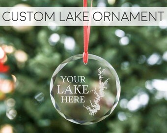 May include: A clear glass Christmas bauble with a red ribbon. The bauble has a white outline of a lake and the text "YOUR LAKE HERE" on it.