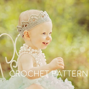 May include: A baby girl wearing a crocheted crown, a white tutu, and a pearl necklace sits on a white chair with a floral patterned seat. The background is a blurred green.
