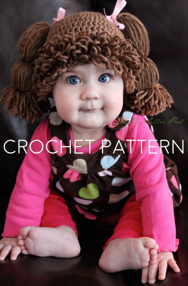 And adorable blue-eyed baby girl is wearing a crochet hat that looks like the yarn hair of a Cabbage Patch Kid doll from the 1980s. It has 2 pigtails and loopy bangs. The photo indicates this is for the crochet pattern to make this hat.