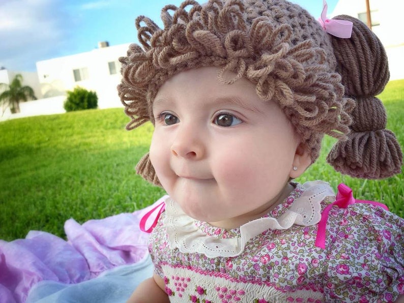 Another brown-eyed adorable baby girl is wearing the light brunette color hat, showing a close-up of the looped bangs and how the hat fits snugly around the head.