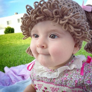 Another brown-eyed adorable baby girl is wearing the light brunette color hat, showing a close-up of the looped bangs and how the hat fits snugly around the head.