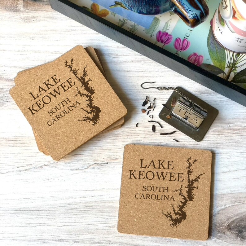 Op de afbeelding: Set van vier kurken onderzetters met een bruine omtrek van Lake Keowee, South Carolina. De onderzetters zijn vierkant en hebben een natuurlijke kurk afwerking.