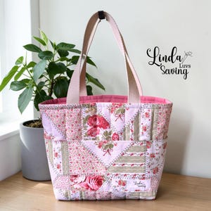 May include: A patchwork tote bag with a floral pattern in shades of pink, red, and beige. The bag has a pink interior and handles. The text "Linda Luvs Sewing" is visible on the bag.