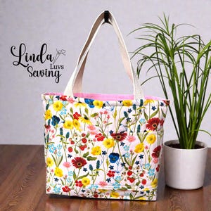 May include: A floral tote bag with a white background and colorful flowers in red, yellow, blue, and pink. The bag has a pink interior and white handles. The text "Linda Luvs Sewing" is on the left side.